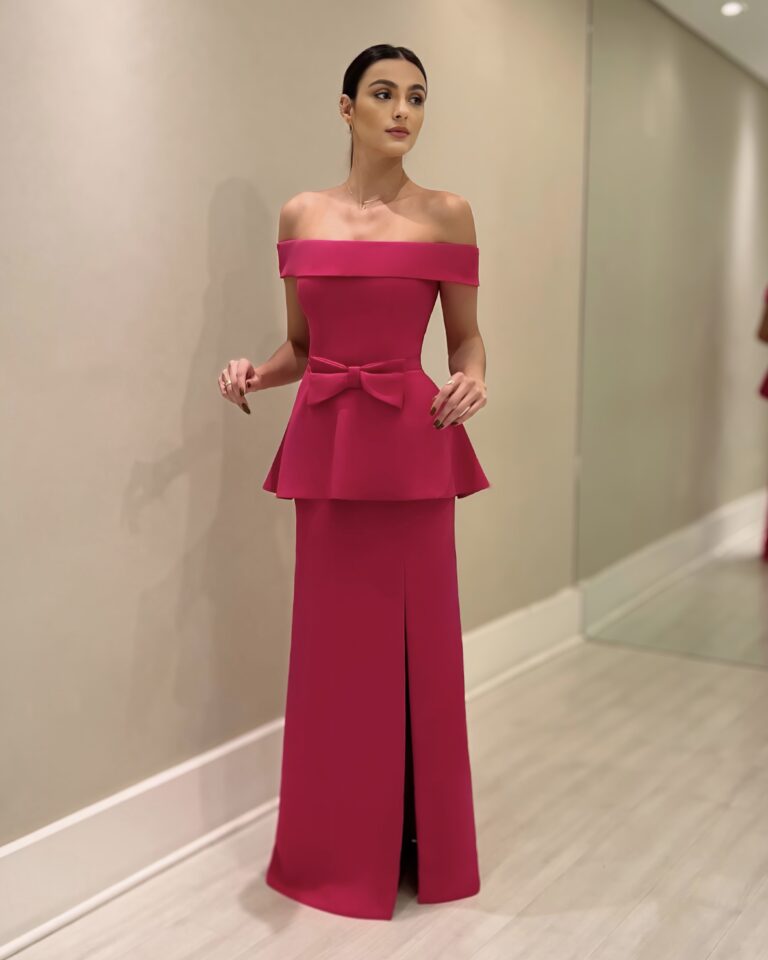 Modelo usando vestido longo pink em crepe com decote ombro a ombro, laço na cintura e fenda frontal